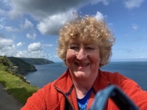 Helen Wilson stands smiling by a coastal scene