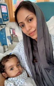 Summiya sits on a hospital bed, holding Yasin. Both are wearing hospital gowns.